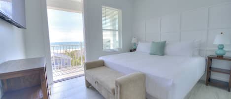 A bedroom with a large bed, a small sofa, a TV, and a balcony with a view.