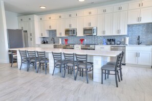 A modern kitchen with white cabinetry, stainless steel appliances, and a large island with bar stools. - BRAND NEW ACROSS FROM OCEAN 12 beds/10 baths • Pvt Pool and Spa • Sleeps 28 (North Myrtle Beach)