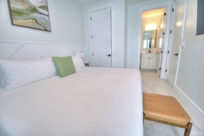 A hotel room with a bed, a bench, a door, a mirror, and a painting on the wall. - BRAND NEW ACROSS FROM OCEAN 12 beds/10 baths • Pvt Pool and Spa • Sleeps 28 (North Myrtle Beach)