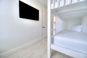 A room with a bunk bed, a white door, and a black screen on the wall. - BRAND NEW ACROSS FROM OCEAN 12 beds/10 baths • Pvt Pool and Spa • Sleeps 28 (North Myrtle Beach)