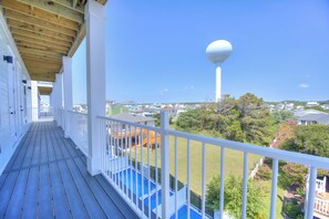 A wooden deck with a pool, white railings, and a view of a town with houses and a water tower. - BRAND NEW ACROSS FROM OCEAN 12 beds/10 baths • Pvt Pool and Spa • Sleeps 28 (North Myrtle Beach)