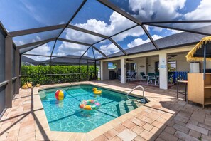 A covered outdoor swimming pool with clear blue water, surrounded by a patio area with seating and a view of the sky. - Turtle Cove | Heated Pool & Waterfront Retreat (Cape Coral)