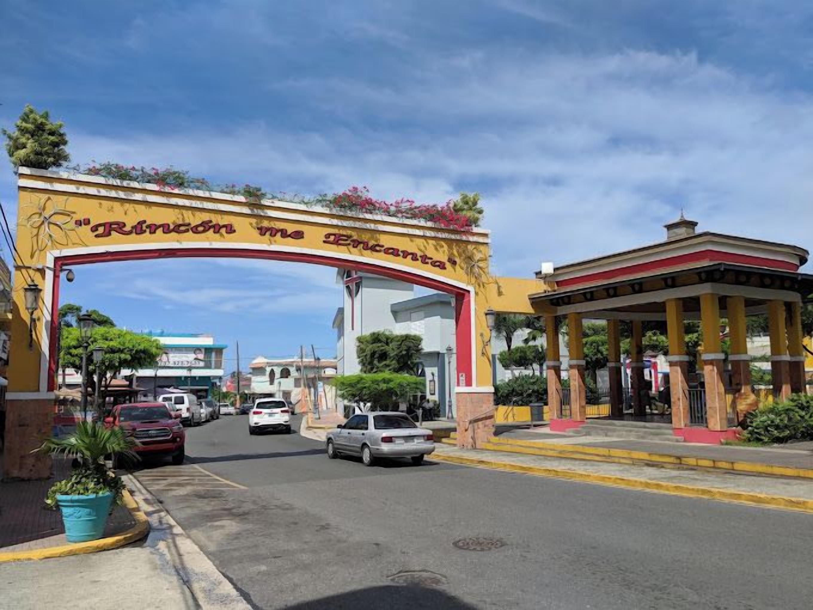 A street entrance with a large archway, a gazebo, and a building with a sign.