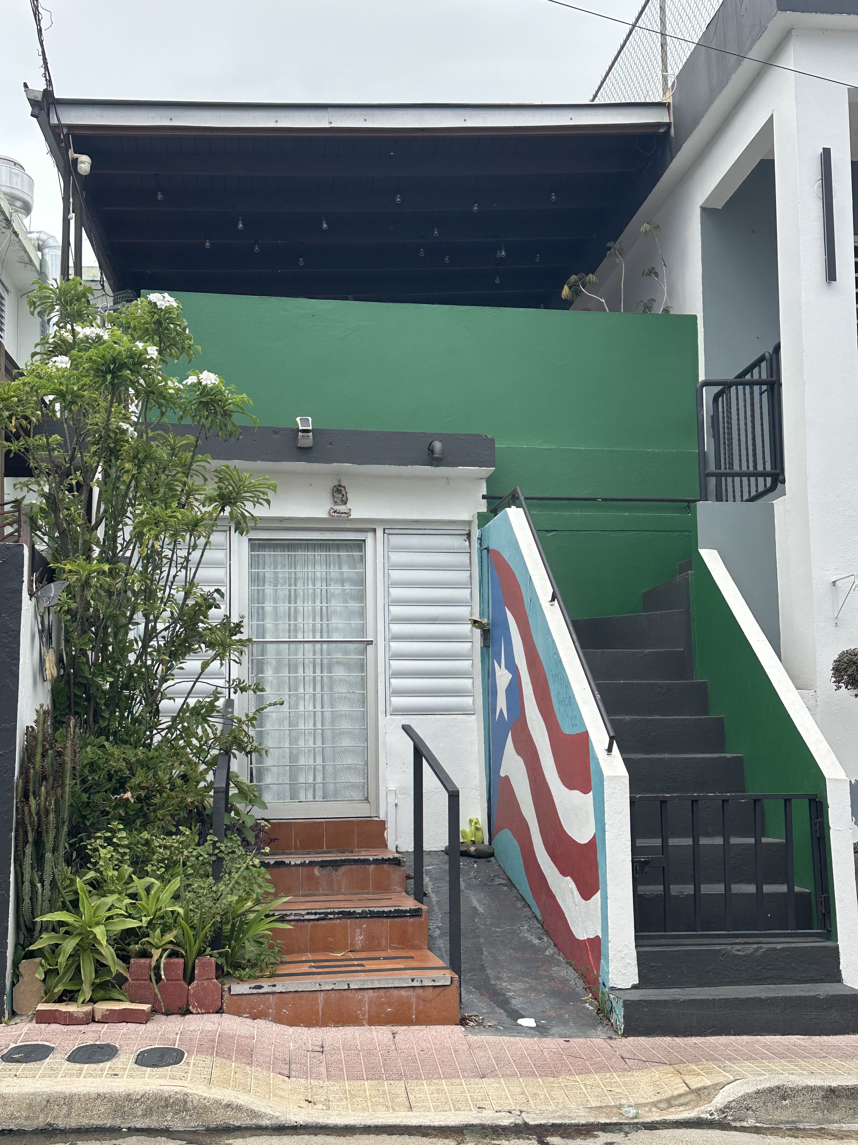 A residential building with a green exterior wall, a white door, and a staircase with a black railing.