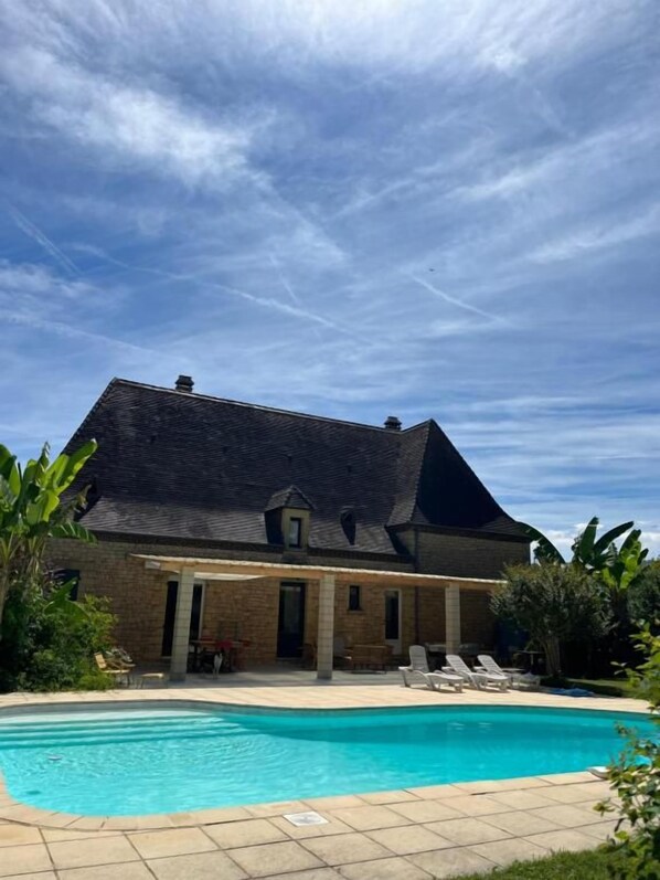 Une maison avec une piscine, un patio couvert et un jardin.