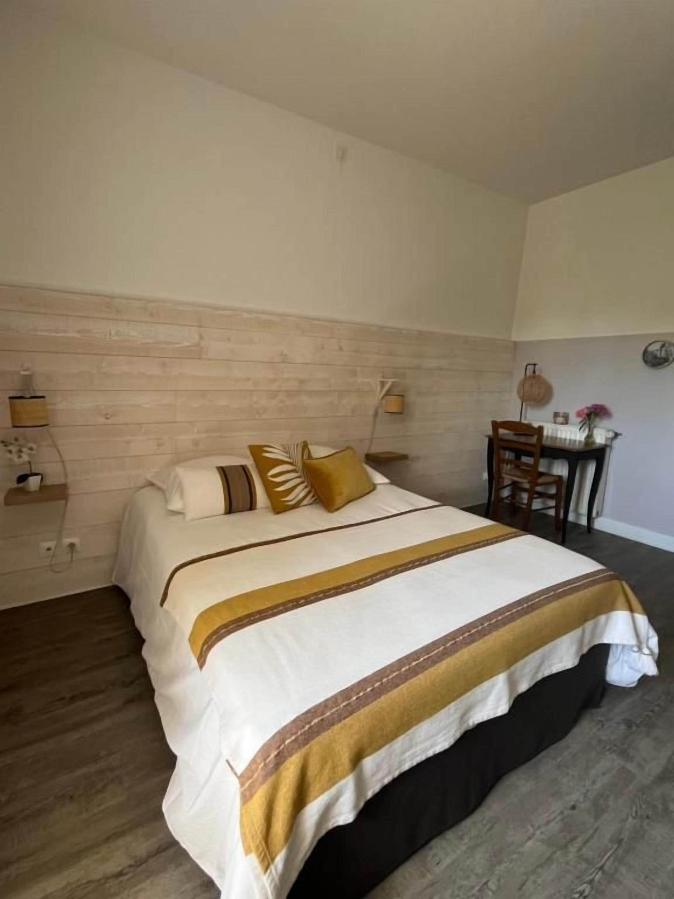 Een hotelkamer met een bed, een houten hoofdbord, een klein tafeltje met een stoel en een wandlamp.