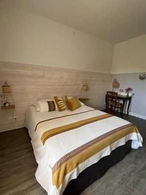 Une chambre d’hôtel avec un lit, une tête de lit en bois, une petite table avec une chaise et une lampe fixée au mur.