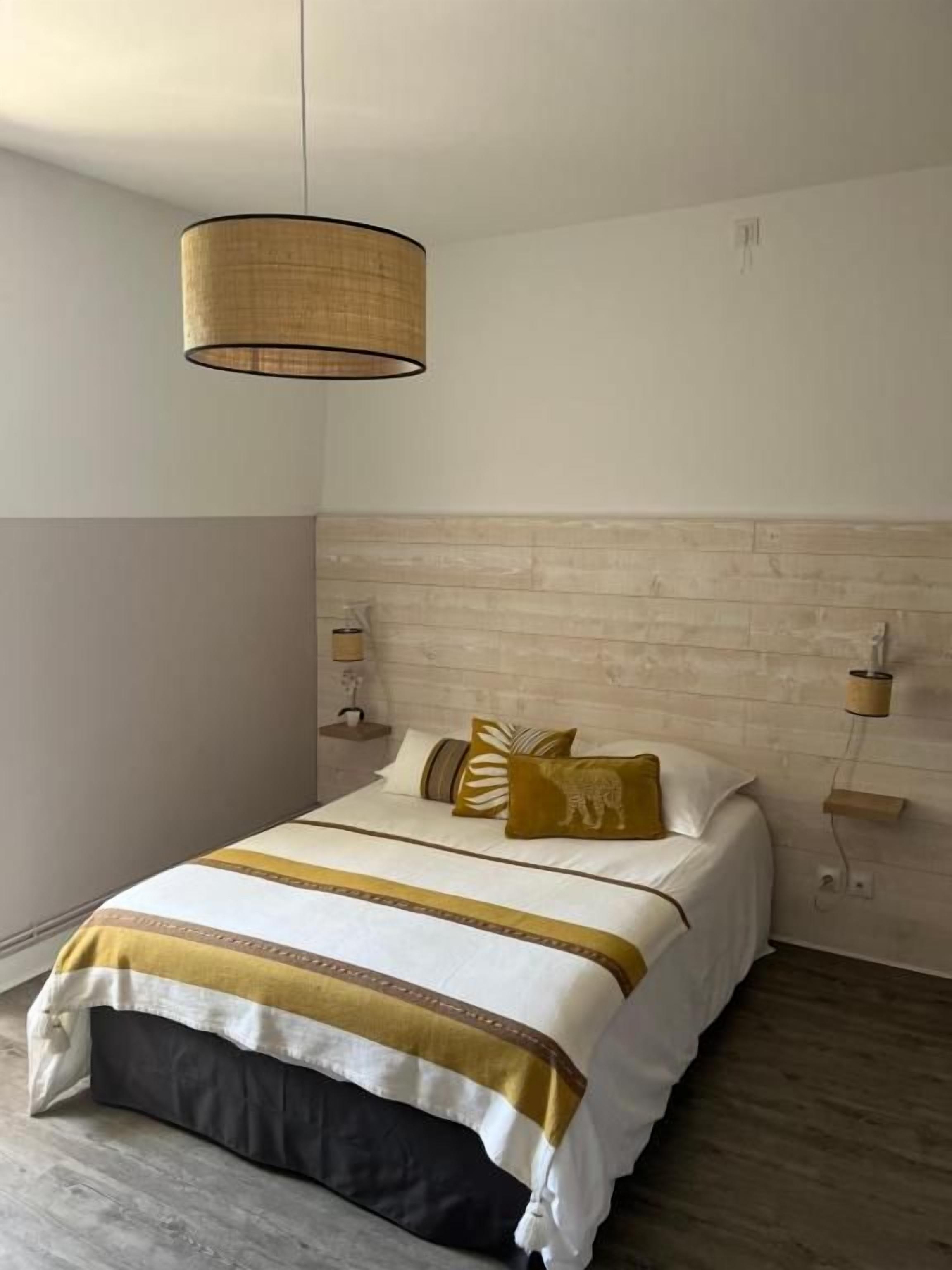 A bedroom with a bed, bedside lamps, a hanging light fixture, and a wooden headboard.