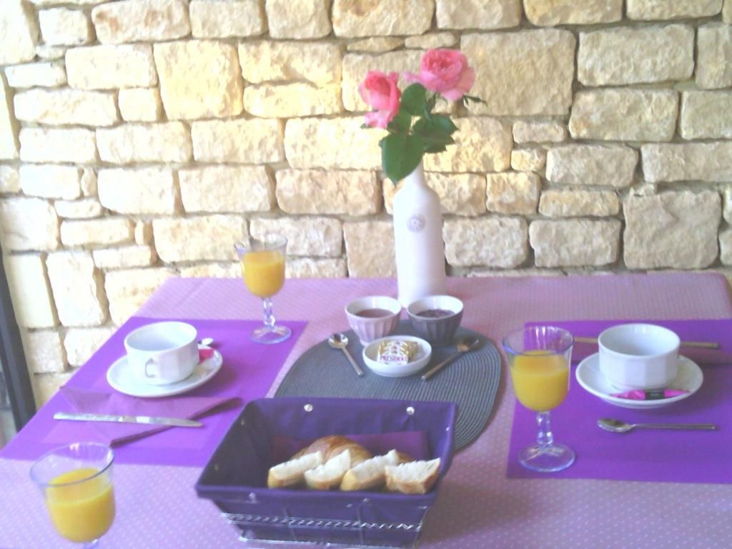 Una mesa de desayuno con un florero de flores, una bandeja de pan y un vaso de jugo de naranja.