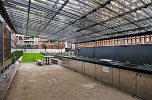 Ein Außenbereich mit einer Terrassenfläche, einem Metalldach, einer langen Theke mit Spüle und einer Bank.