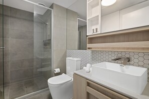 Ein modernes Badezimmer mit Duschkabine aus Glas, Toilette, Waschbecken und Spiegel.
