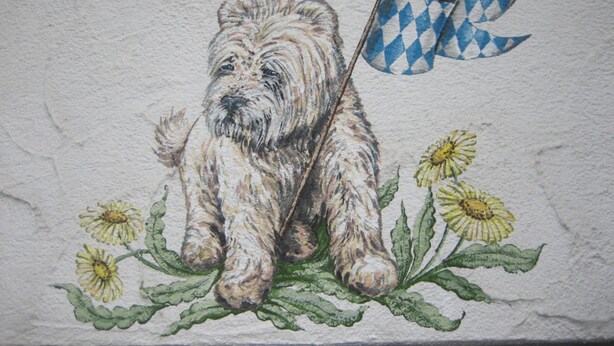 A wall with a painting of a dog with a flag. - Grieshaber Haisl (Bad Bayersoien)