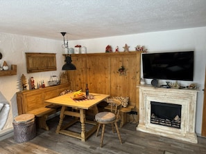 A cozy room with a wooden dining table, benches, a fireplace, a television, and holiday decorations. - Grieshaber Haisl (Bad Bayersoien)