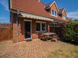 A residential property with a brick exterior, a covered patio with a table and chairs, and a fenced backyard. - House Section 152a "At the Lighthouse" (St. Peter-Ording)
