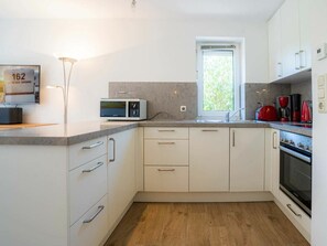 A modern kitchen with white cabinets, a microwave, a red kettle, and a window providing natural light. - House Section 152a "At the Lighthouse" (St. Peter-Ording)