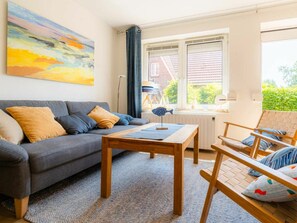 A living room with a grey sofa, a wooden coffee table, and a chair with striped cushions. - House Section 152a "At the Lighthouse" (St. Peter-Ording)