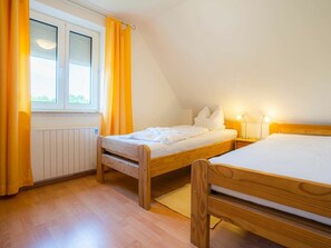 A room with two wooden beds, a window with curtains, a radiator, and a nightstand with a lamp. - House Section 152a "At the Lighthouse" (St. Peter-Ording)