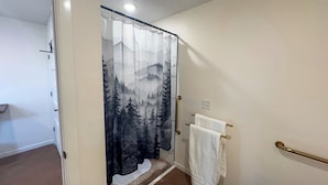 A bathroom with a shower curtain featuring a forest design, a towel rack with a white towel, and a handrail. - Quaint Cabin on 30 acres in Springfield (Springfield)