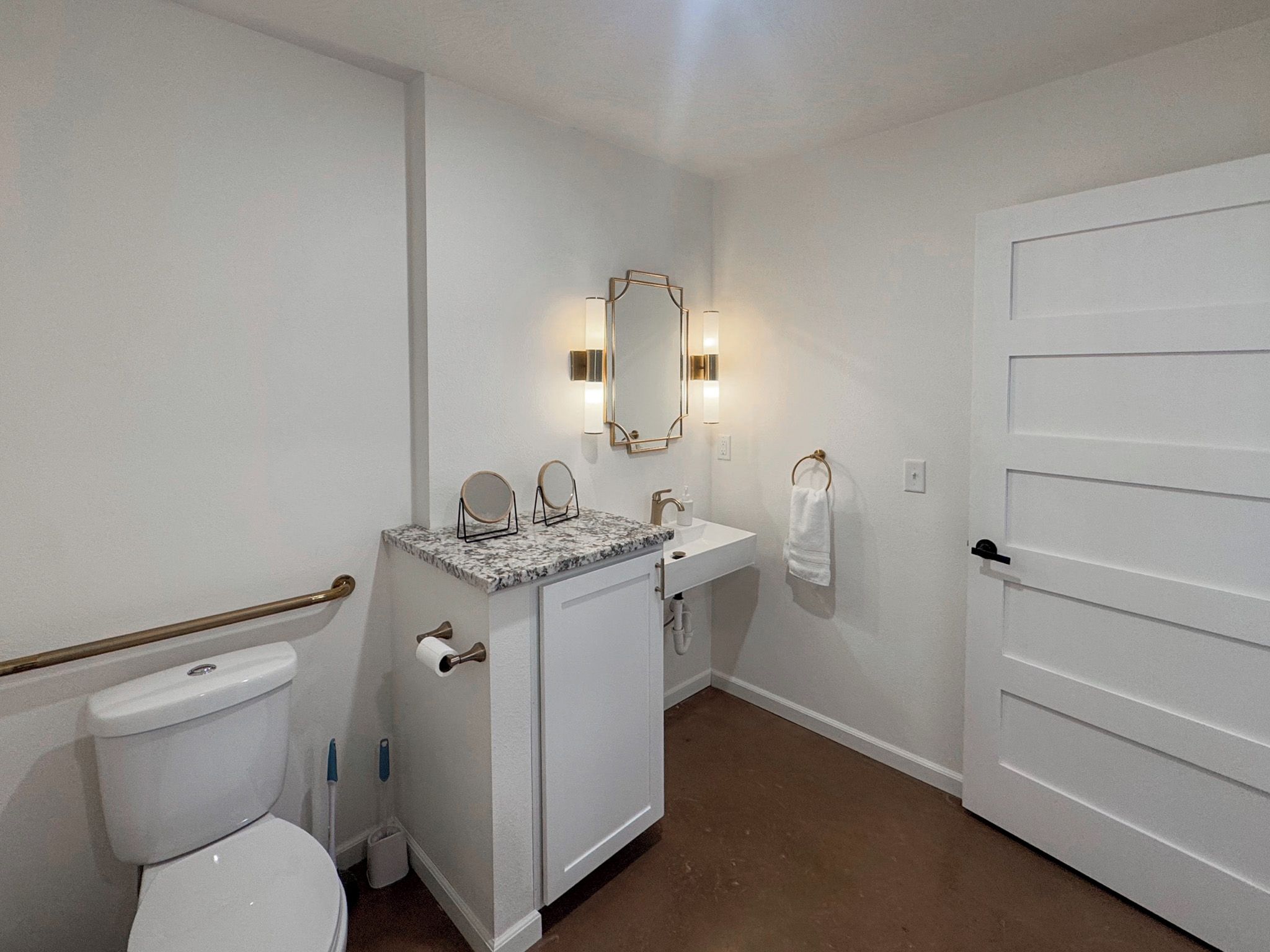 A bathroom with a toilet, sink, vanity, and a mirror with wall sconces.