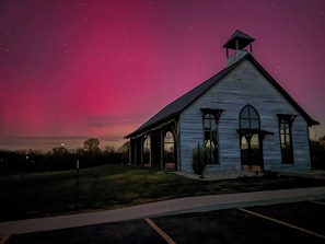 Uma igreja branca com um campanário, janelas amplas e um alpendre sob um céu crepuscular.