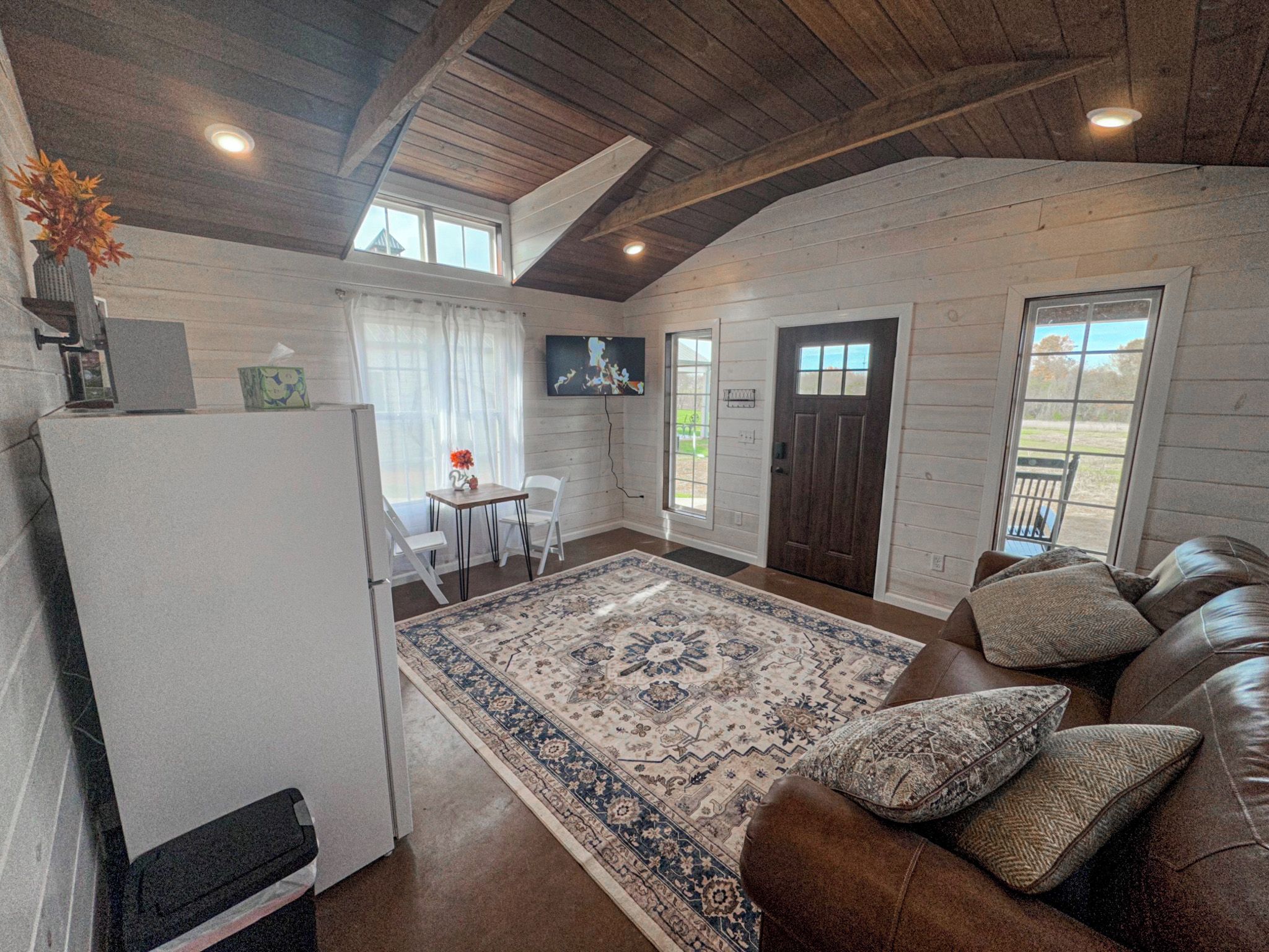 A cozy interior with a brown leather sofa, a patterned rug, and a wooden ceiling.