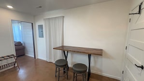 A room with a wooden table and two stools, a white door, and a window with curtains. - Quaint Cabin on 30 acres in Springfield (Springfield)