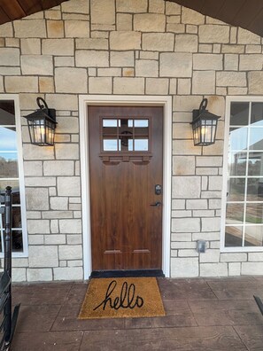 A stone facade with a wooden door, two wall-mounted lanterns, and a doormat with 'hello' written on it.