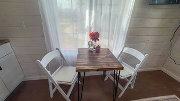 Een eethoek met een houten tafel en twee witte stoelen, een vaas met bloemen en uitzicht door dunne gordijnen.