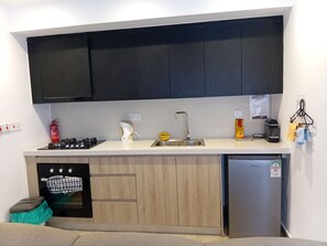 Eine moderne Küche mit schwarzen Schränken, einer Edelstahl-Spüle, einer Kaffeemaschine und einem kompakten Kühlschrank.