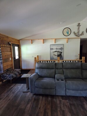 A living room with a gray sofa, a wooden bench, a painting of a boat, and a wall-mounted anchor decoration. - Spacious 7-bedroom house in serene Arkdale with AC (Arkdale)