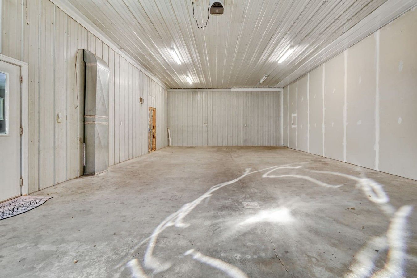 Um espaço amplo e vazio com paredes brancas e chão de concreto, com uma porta e uma pequena janela.