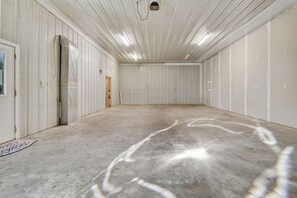 A large, empty room with white walls and a concrete floor, featuring a single door and a small window.