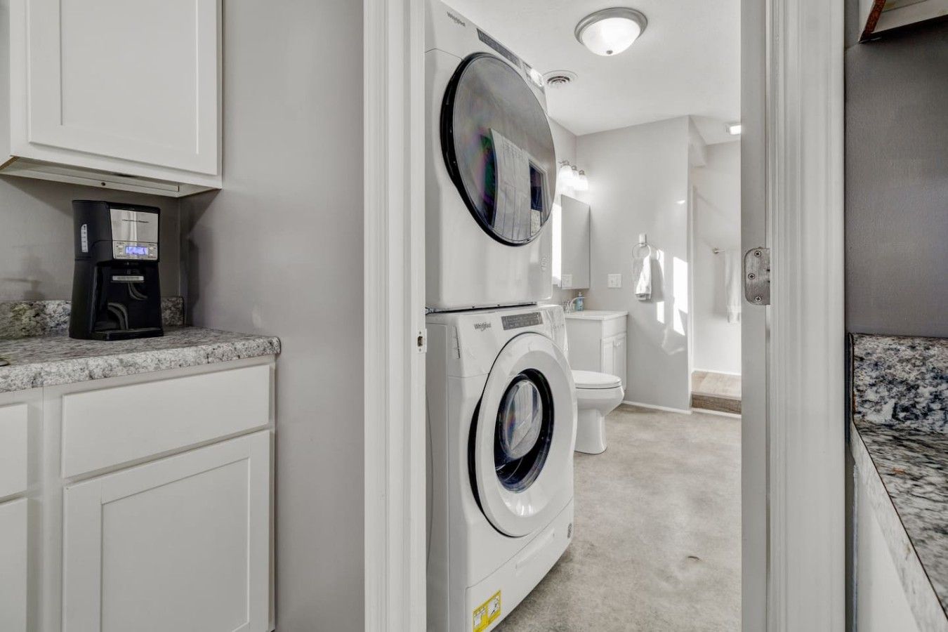 A laundry room with a washing machine and dryer, a coffee maker, and a bathroom with a toilet and sink.