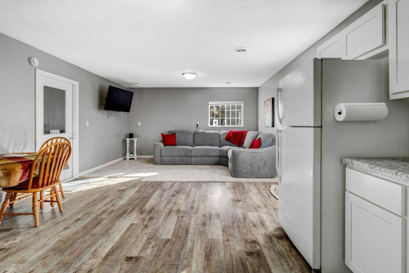 Una cocina moderna con armarios blancos, un refrigerador gris y un comedor con mesa y sillas de madera.