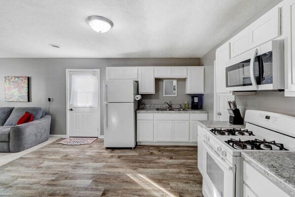 A compact kitchen with white cabinets, a refrigerator, a stove, and a microwave.