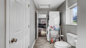 Een smalle gang die uitkomt bij een badkamer met toilet, een witte deur en een raam.