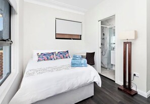 Ein Hotelzimmer mit Bett, Fenster, einer Tür zu einem Badezimmer und einer Stehlampe.