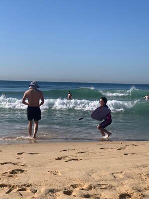 Eine Strandansicht mit Menschen in der Nähe des Wassers, einem klaren Himmel und Fußspuren im Sand.