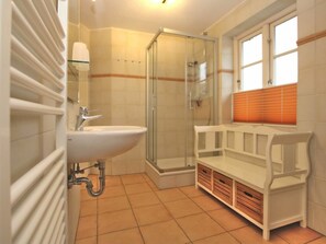 Ein Badezimmer mit Duschkabine aus Glas, einem weißen Waschbecken und einer Sitzbank mit Stauraum.