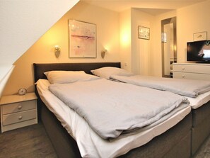 Ein Hotelzimmer mit Bett, Nachttischen, einem Fernseher und Kunstwerken an den Wänden.