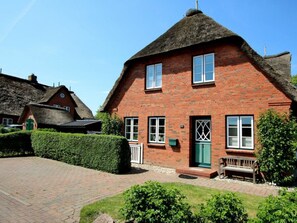 Ein rotes Backsteinhaus mit einem Reetdach, einer grünen Tür und einer Bank davor.
