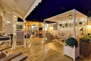 An outdoor patio area with wooden flooring, white furniture, and a covered seating area. - Luxury Villa Costabella Marbella—Pool, Jacuzzi, and Sauna—400 m from the Beach (Marbella)