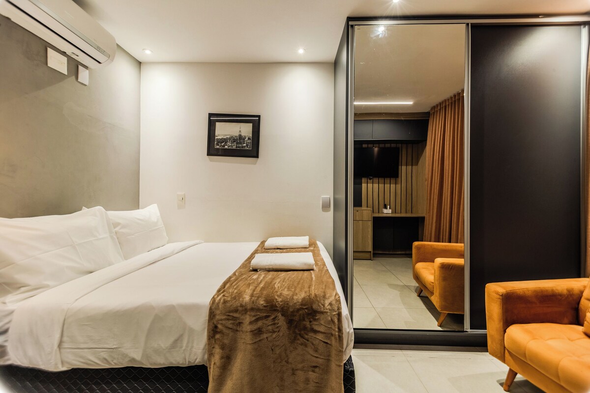 Quarto de hotel com uma cama, uma escrivaninha, uma cadeira e uma porta deslizante para um banheiro.