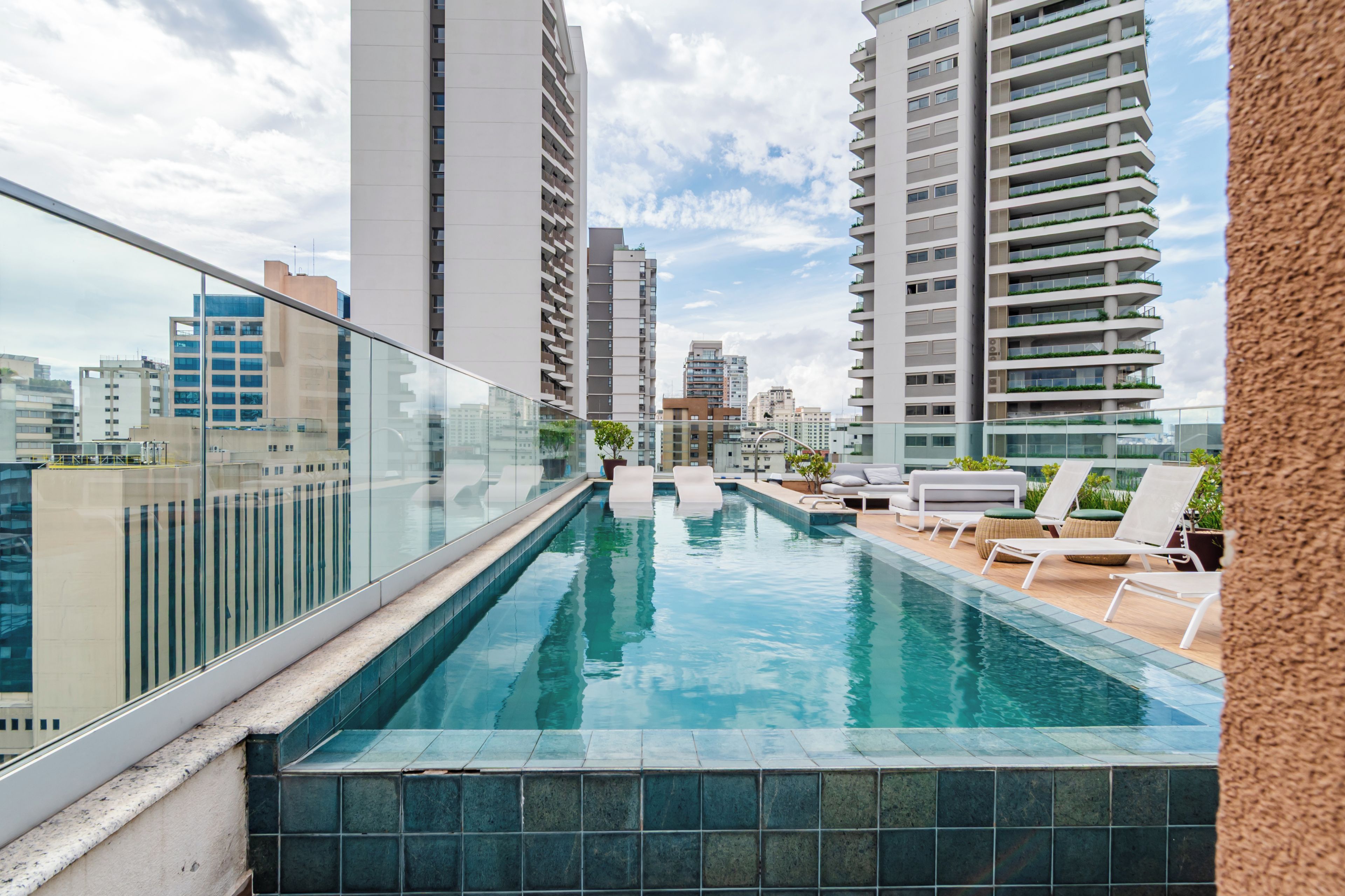Piscina no terraço com espreguiçadeiras e guarda-corpo de vidro com vista para a cidade.