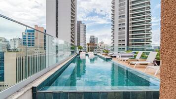 Piscina no terraço com espreguiçadeiras e guarda-corpo de vidro com vista para a cidade.