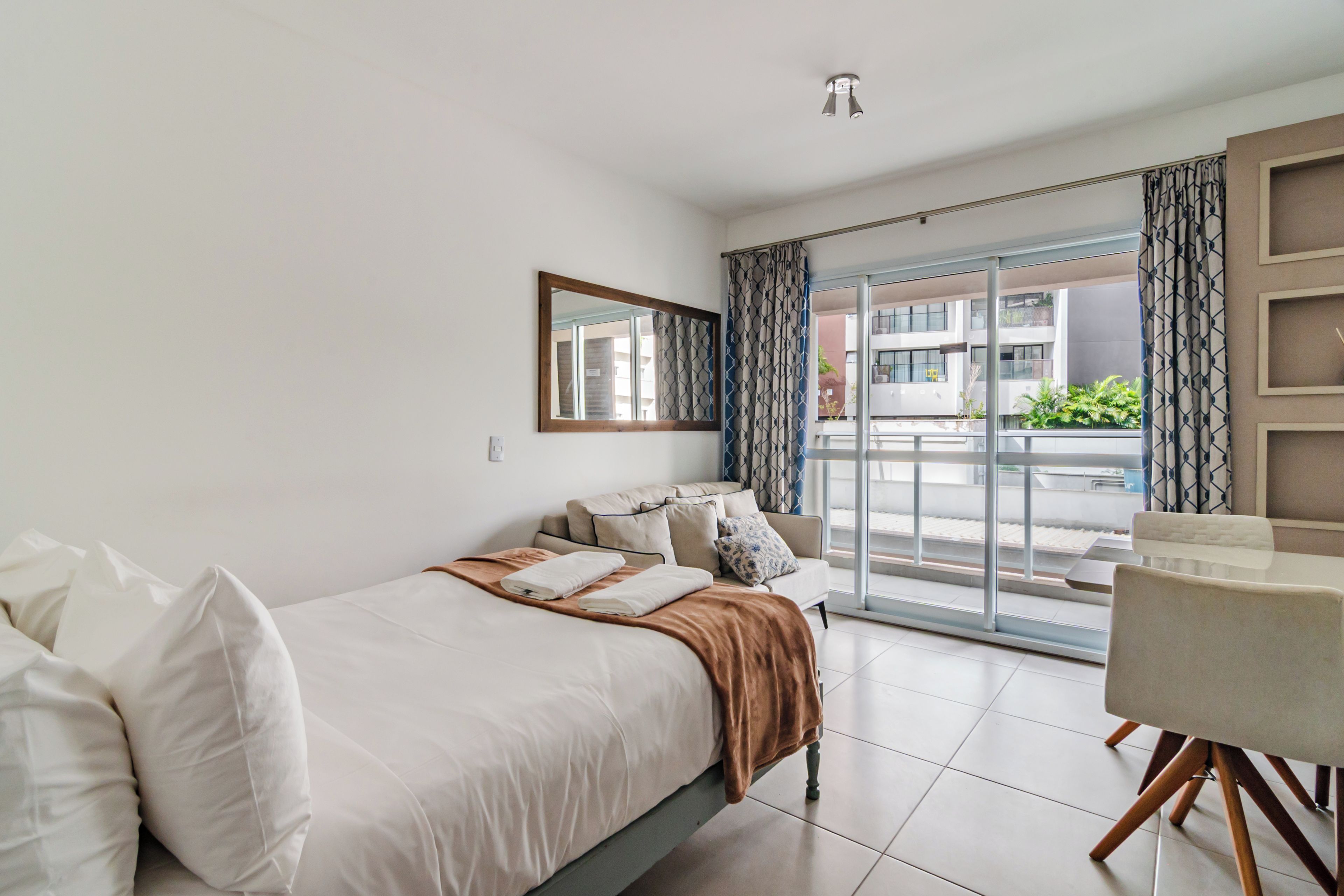 Quarto de hotel com cama, poltrona, janela grande e varanda.