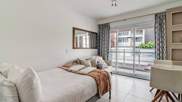 Quarto de hotel com cama, poltrona, janela grande e varanda.