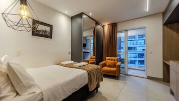 Quarto de hotel moderno com cama, poltrona, espelho grande e vista para a cidade.