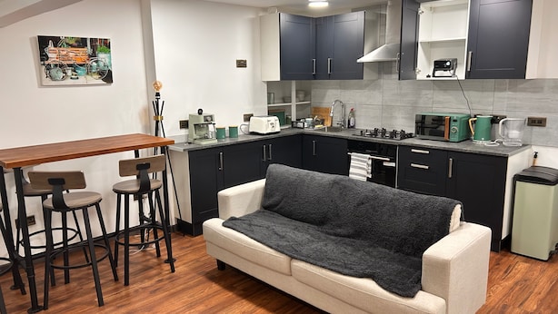 A compact kitchen with dark cabinets, a wooden dining table, and a sofa. - Pottery District 1-bed Apt, Sleeps 3 & Wifi (Stoke-on-Trent)