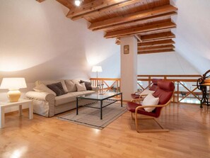A spacious living room with a high wooden ceiling, a sofa, a red chair, a coffee table, and a lamp. - Holiday Home With 2 Bedrooms (St. Peter-Ording)